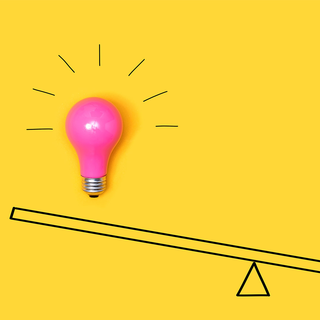 Pink lightbulb on a seesaw type scale with a yellow background